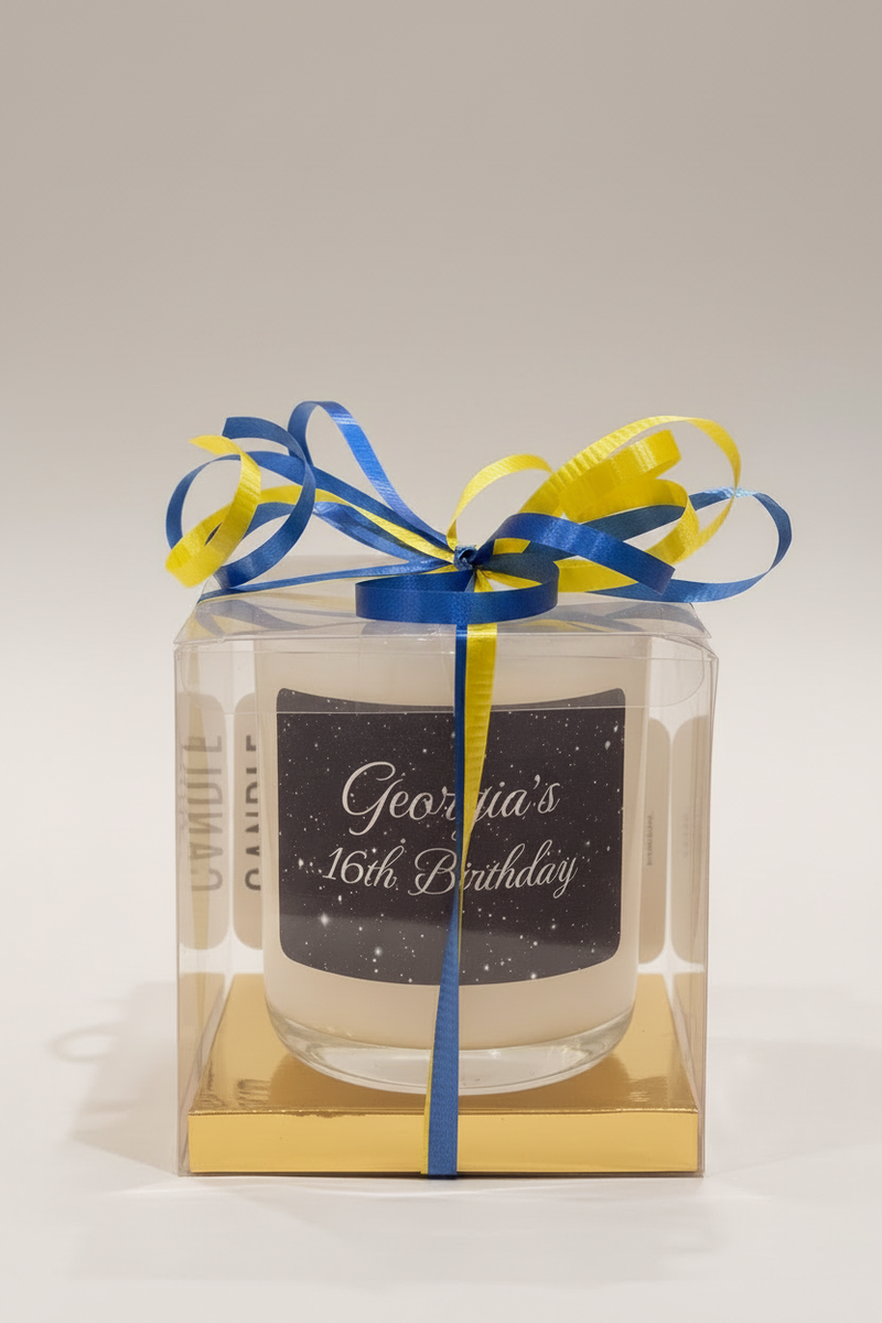 Candle in a clear box with blue and yellow ribbons and a personalized label on a light gray background