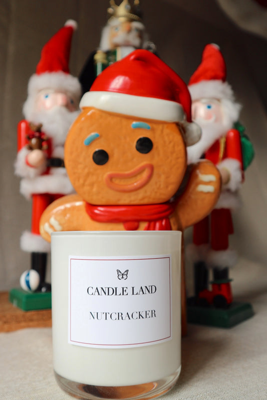 A decorative gingerbread man candle holder with a 'Nutcracker' label, placed in front of a Christmas-themed backdrop with Santa hats.
